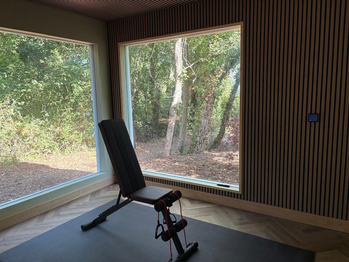 Black weight bench in modern room with large windows overlooking forest trees and natural foliage