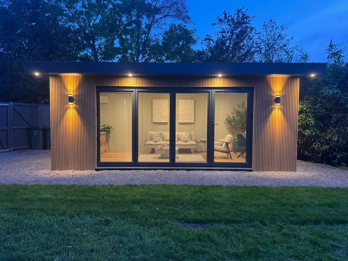 Contemporary garden office with corrugated metal walls and large glass doors illuminated at dusk