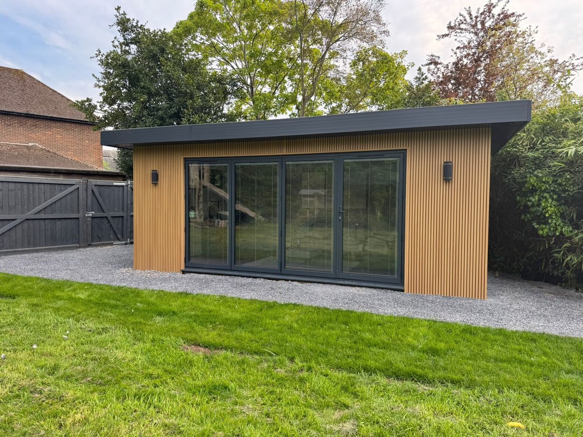 Modern garden studio with timber cladding, large black-framed sliding doors, and gravel base in a residential backyard