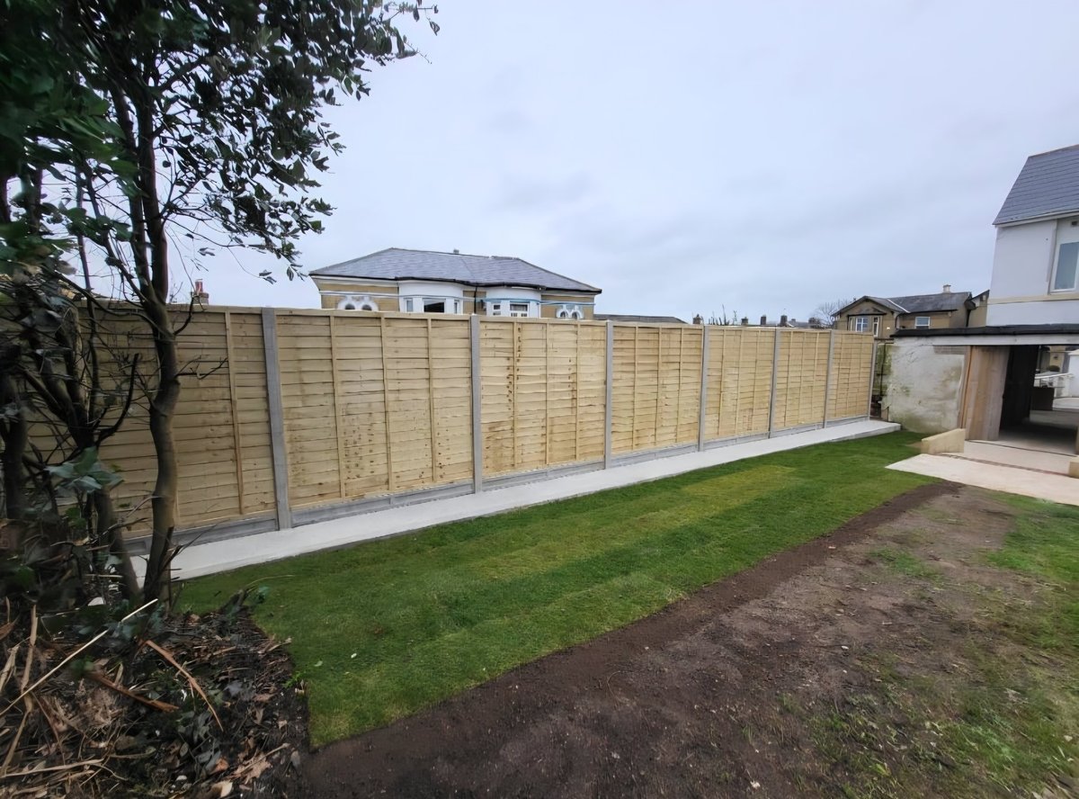Newly installed wooden fence panels in a residential backyard with green lawn and houses in the background