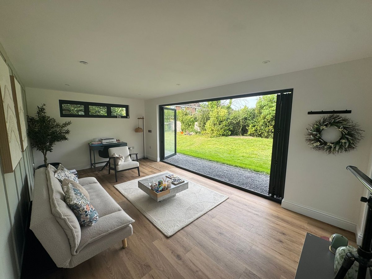 Modern living room with white sofa, wooden flooring, and large glass doors opening to a green garden view