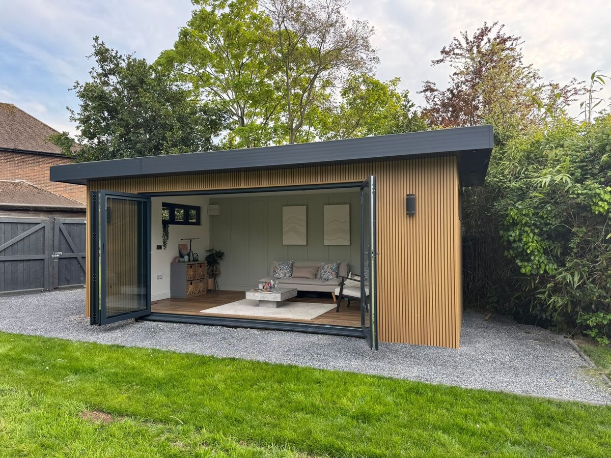 Modern garden room with black frame and wooden siding, featuring large open glass doors and contemporary interior seating area