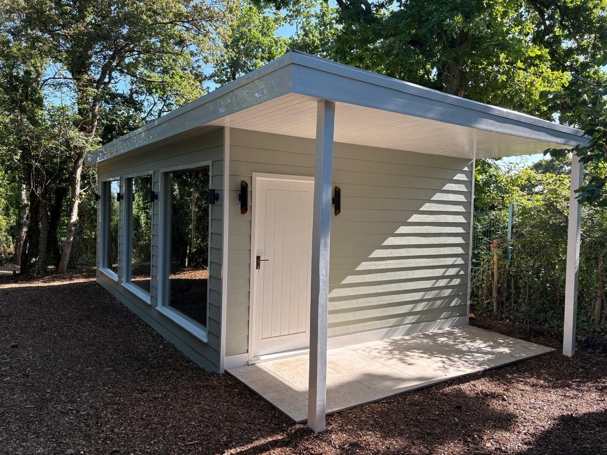 Modern shed with large windows and covered porch area surrounded by trees in a wooded setting